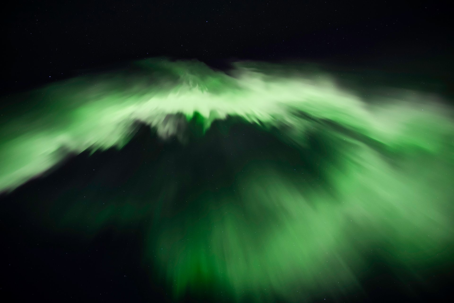 Green aurora stretching across the sky with mountain silhouette