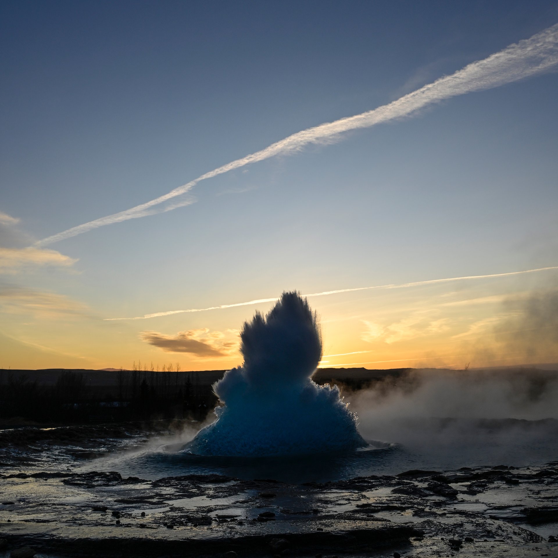 Strokkur geyser erupting with steaming geothermal landscape at Geysir area